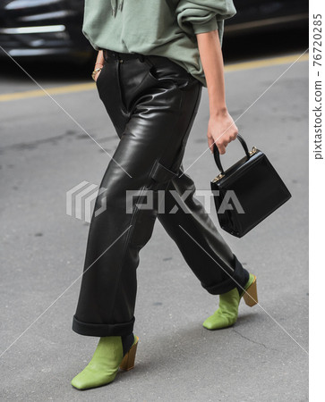 Detail of a fashionable outfit woman wearing green shoes, black handbag and black leather pants 76720285