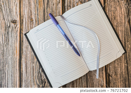 Opened diary or notebook for notes with pen on wooden table top view 76721702