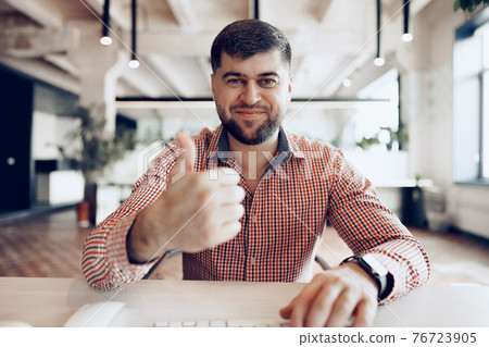 Joyful young businessman sitting at desk looking at camera Joyful young businessman sitting at desk looking at camera 76723905