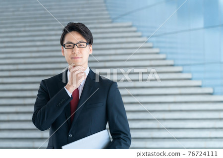 A businessman in a suit with a computer smiling in the office A businessman in a suit with a computer smiling in the office 76724111