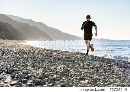 Man running on the beach, mountains background Man running on the beach, mountains background 76724649