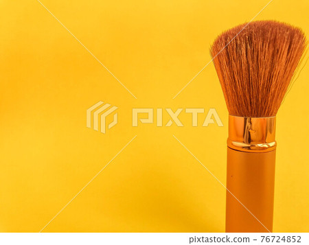 Beautiful fashionable beauty cosmetic glamorous white and gold brushes and brushes for applying makeup and powder and cosmetics on the face on a yellow gentle background. Flat lay Beautiful fashionable beauty cosmetic glamorous white and gold brushes and brushes for applying makeup and powder and cosmetics on the face on a yellow gentle background. Flat lay 76724852