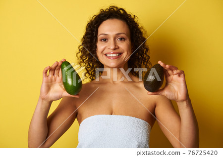 Curly-haired mixed race woman holding two ripe avocado fruits and smiling with toothy smile, isolated over yellow background with space for text Curly-haired mixed race woman holding two ripe avocado fruits and smiling with toothy smile, isolated over yellow background with space for text 76725420
