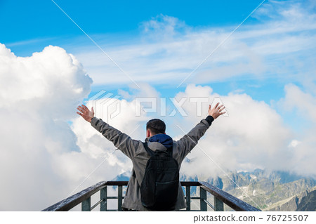 Tourist standing on the observation deck and enjoying of amazing view of mountains peak and clouds 76725507