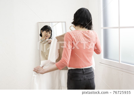 一個女人一邊照鏡子一邊選擇穿什麼衣服 76725935