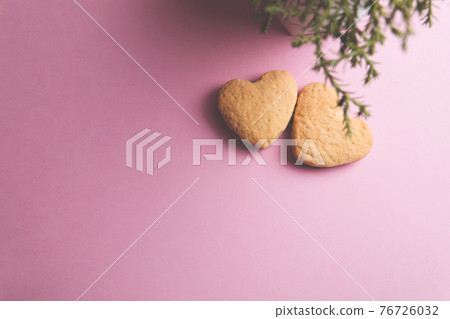 Two cookies in shape of a heart next to each other on a pink background. The concept of Valentine's Day. Two cookies in shape of a heart next to each other on a pink background. The concept of Valentine's Day. 76726032