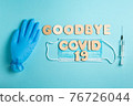 Words GOODBYE COVID 19 and syringe, inflated medical glove and facemask. vaccine and the end of epidemic concept. 76726044