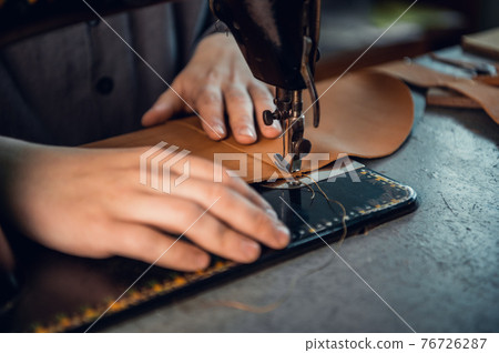 The process of stitching two pieces of genuine leather by a shoemaker on a special old-school sewing machine. Stitches of thread and the hand of the master 76726287