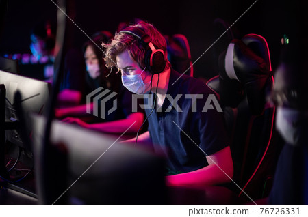 White-skinned and black-skinned guys are members of an esports online strategy crew. Play at the computer at an international tournament during the pandemic. White-skinned and black-skinned guys are members of an esports online strategy crew. Play at the computer at an international tournament during the pandemic. 76726331