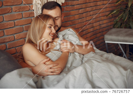Couple sitting on a bed in a room Couple sitting on a bed in a room 76726757