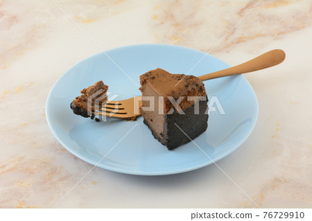 Slice of Belgian chocolate cheesecake with missing bite and copper fork on blue dessert plate 76729910