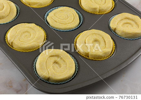 Raw swirl corn muffin dough in silicone muffin cups in muffin pan Raw swirl corn muffin dough in silicone muffin cups in muffin pan 76730131