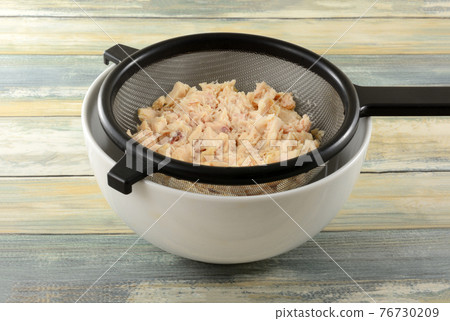 Rinsed canned albacore tuna draining in strainer into white bowl Rinsed canned albacore tuna draining in strainer into white bowl 76730209