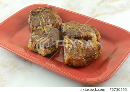 Four baked lamb chops with spice rub on red serving plate Four baked lamb chops with spice rub on red serving plate 76730363