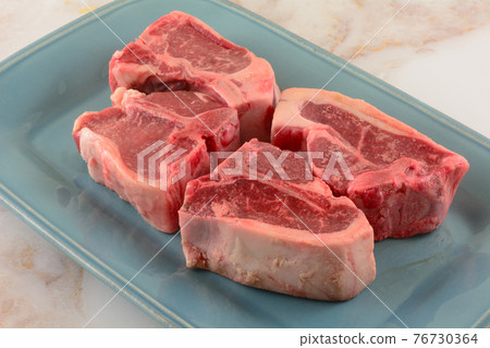 Four raw lamb chops on blue plate in preparation for grilling roasting or baking Four raw lamb chops on blue plate in preparation for grilling roasting or baking 76730364