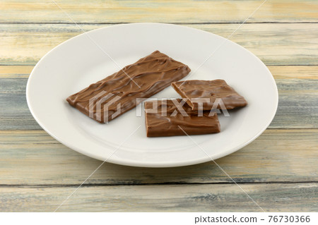 Candy bar of almond caramel covered in rich milk chocolate and pieces on white snack plate 76730366