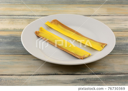 Two banana toffee taffy candy strips on white snack plate 76730369
