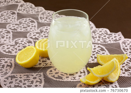 Drinking glass of lemonade with lemon wedges and lemon haves on lace heart table runner o brown tablecloth 76730670