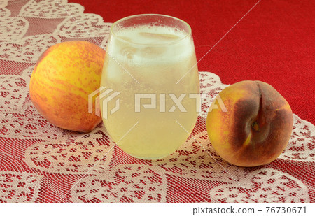 Mocktail of peach juice and lemon lime soda pop in drinking glass and fresh raw peaches on pink heart lace table runner on red tablecloth Mocktail of peach juice and lemon lime soda pop in drinking glass and fresh raw peaches on pink heart lace table runner on red tablecloth 76730671