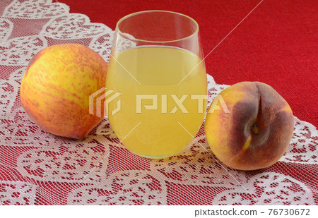 Peach juice in drinking glass and fresh raw peaches on pink heart lace table runner on red tablecloth 76730672