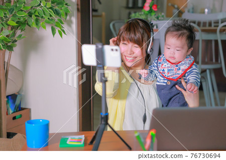 嬰兒拉著耳機和女性參加智能手機在線會議 嬰兒拉著耳機和女性參加智能手機在線會議 76730694