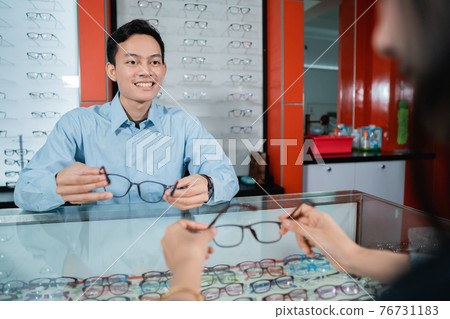 an eye clinic employee is serving female consumers when choosing glasses to use 76731183