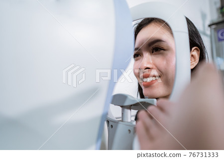 A beautiful woman is undergoing an examination using an eye examiner 76731333