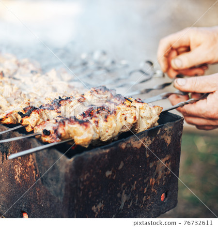 Shashlyk preparing outdoor, man's hands coocking kebab, russian meat in garden, coocking on grill. 76732611