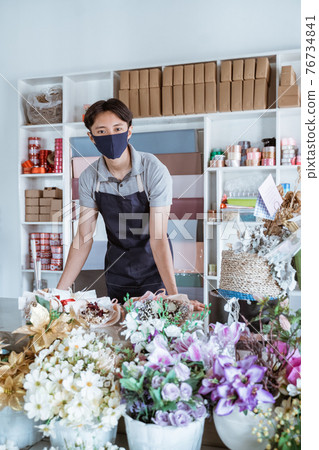 florist man wearing face mask standing behind a flower bouquet 76734841