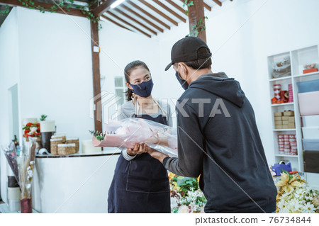 young female shopkeeper wearing a face mask and apron. servicing male flannel flower buyers young female shopkeeper wearing a face mask and apron. servicing male flannel flower buyers 76734844