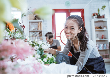 happy young couple wearing apron smiling looking at camera. working in flower shop happy young couple wearing apron smiling looking at camera. working in flower shop 76734847