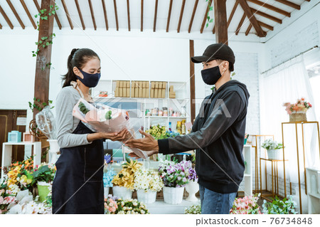 smiling young female shopkeeper wearing a face mask and apron. servicing male flannel flower buyers smiling young female shopkeeper wearing a face mask and apron. servicing male flannel flower buyers 76734848