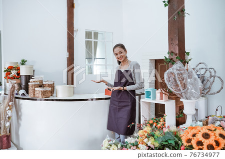 young female florist wearing apron standing in front office smiling looking at the camera. 76734977