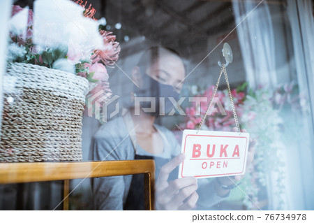 young woman florist wearing an apron and face mask setup the sign in front of the door young woman florist wearing an apron and face mask setup the sign in front of the door 76734978