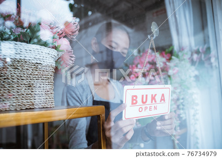 young woman florist wearing an apron and face mask setup the sign in front of the door young woman florist wearing an apron and face mask setup the sign in front of the door 76734979