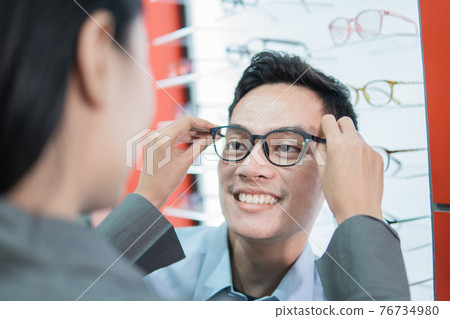 a lady shop assistant puts new glasses on to a male customer a lady shop assistant puts new glasses on to a male customer 76734980
