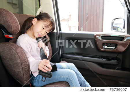 A girl wearing a seatbelt with a junior seat attached to the passenger seat 76736097