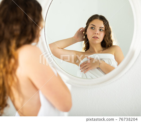 Young long-haired girl admiring her reflection in mirror 76738204