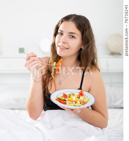 Young attractive smiling woman eating salad for breakfast Young attractive smiling woman eating salad for breakfast 76738245