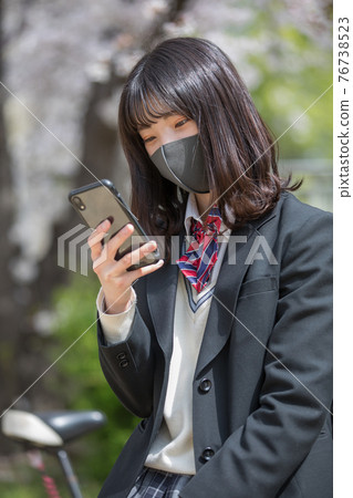High school girl looking at a smartphone on the way to school High school girl looking at a smartphone on the way to school 76738523