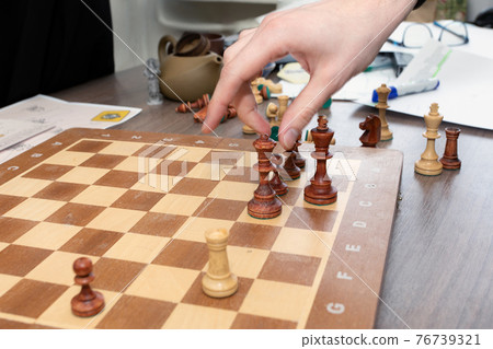 Desk with spread out chessboard and chess pieces, hand about to make next move. Planning course. 76739321