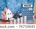 Both hands were holding a house and a calculator, and coins stacked in front of. 76739685