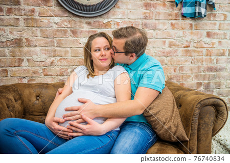 A man kissing his pregnant woman. A man kissing his pregnant woman. They are sitting. 76740834