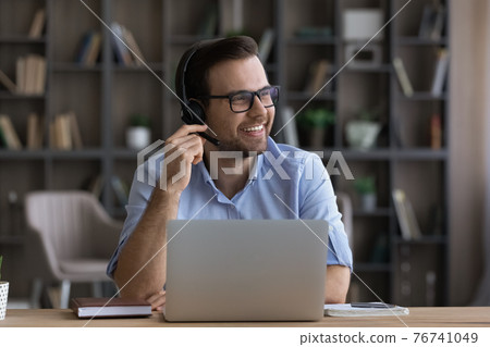 Smiling male employee in headphones use computer thinking Smiling male employee in headphones use computer thinking 76741049