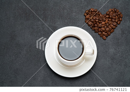 Cup of espresso and Heart shaped roasted coffee beans on dark concrete background 76741121