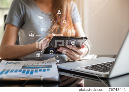 Designer using tablet with laptop and document on desk in office with virtual interface graphic icons network diagram. 76742441