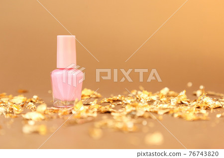 Nail polish small glass bottle and gold paper pieces on golden background. Unbranded mockup with copy space. Professional manicure concept. Nail polish small glass bottle and gold paper pieces on golden background. Unbranded mockup with copy space. Professional manicure concept. 76743820