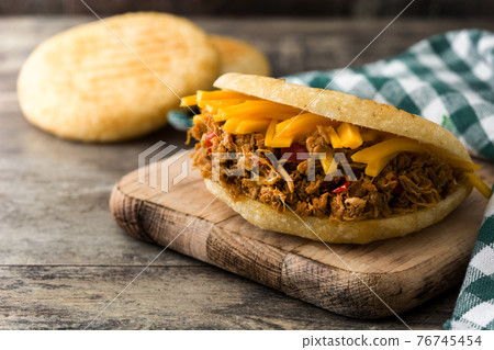 Arepa with shredded beef and cheese on wooden background. 76745454