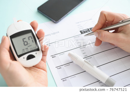 Patient holding glucometer and recording data in diary closeup Patient holding glucometer and recording data in diary closeup 76747521