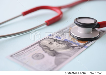 Red stethoscope lying on american dollar bill closeup Red stethoscope lying on american dollar bill closeup 76747523
